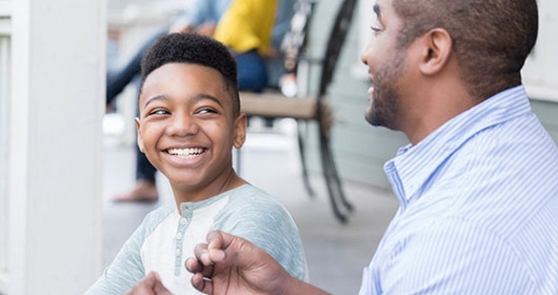 Young Black child smiles while sitting on a porch with an adult male of color.