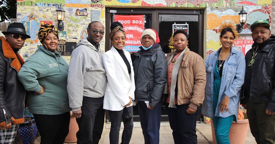 A group of eight Black men and women stand together — smiling — in front of a local business.