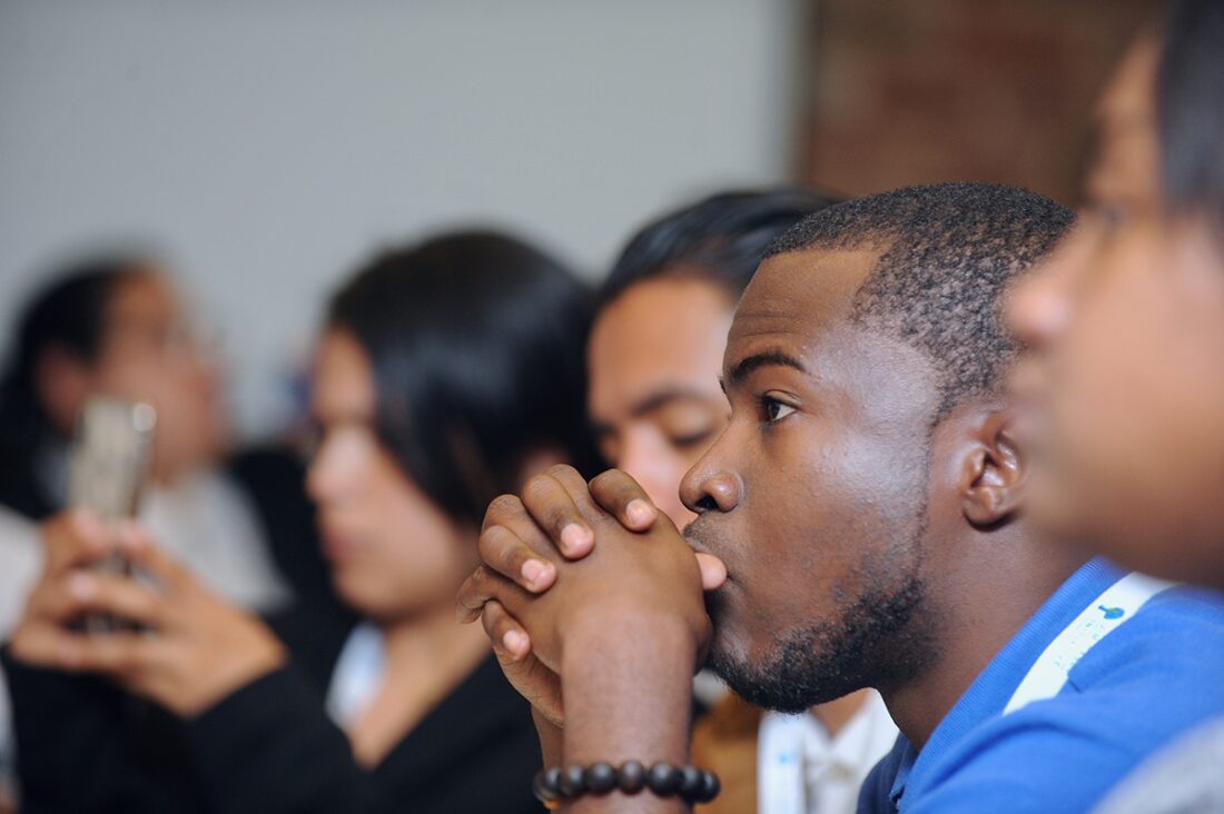 Young people of color sitting in a row, as camera captures sides of faces