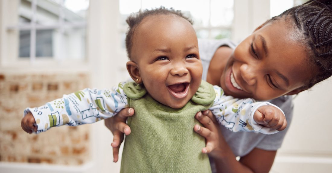 Black mother holds up her infant; both wear big smiles