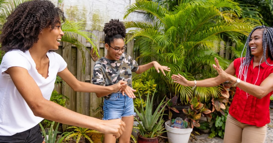 Two teenage African American sisters dancing with their mother in the backyard in Miami