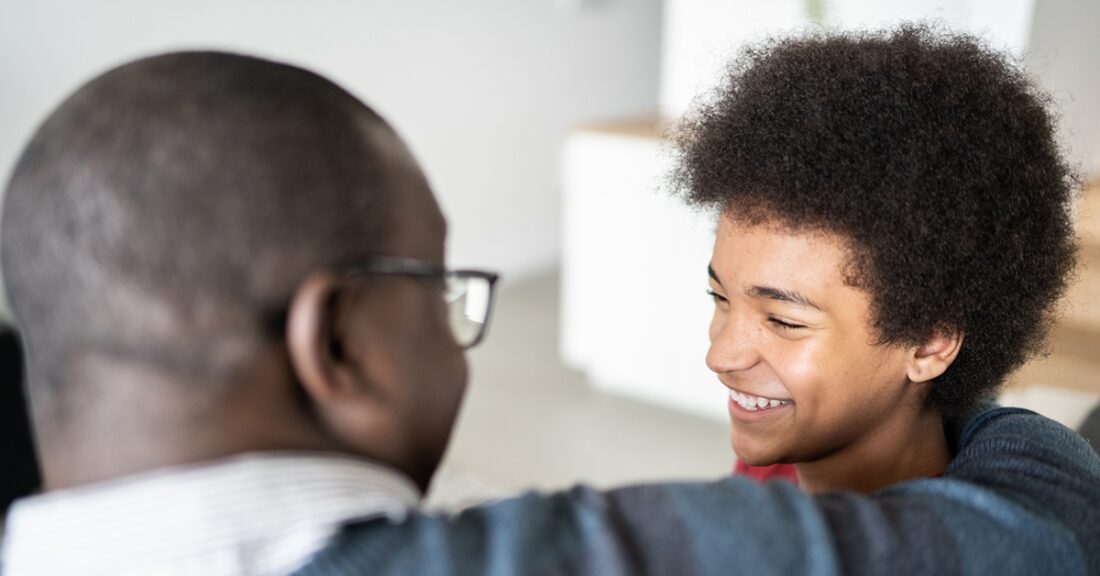 A young Black man sits smiling at an older Black man.