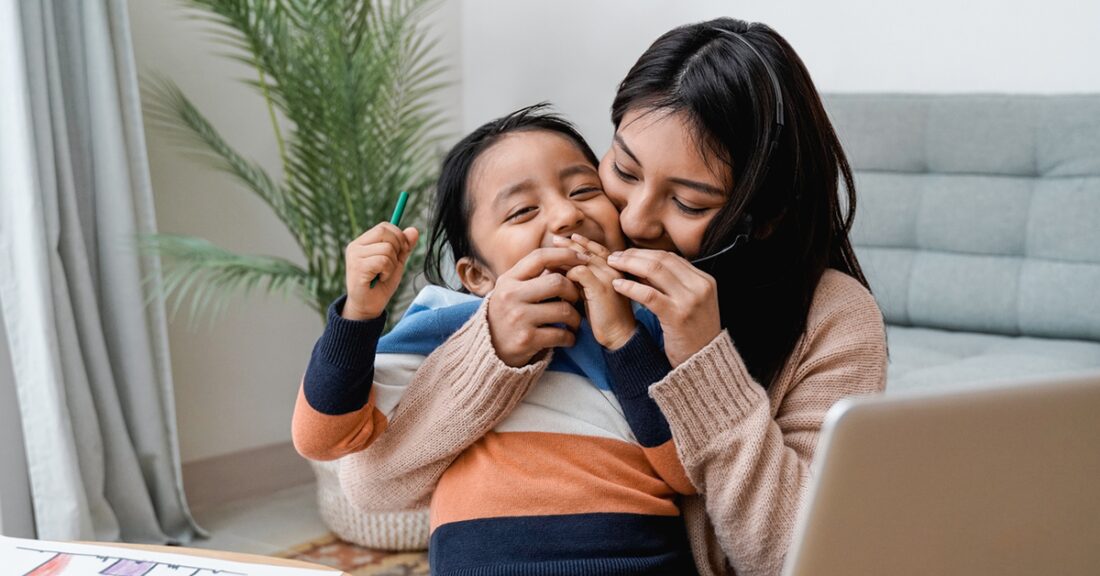 A young Hispanic mother smiles while cuddling her young child.