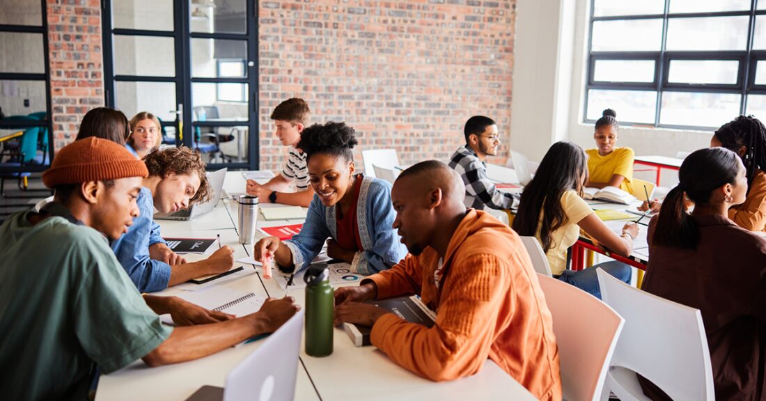 A group of racially diverse young people sit at tables, talking