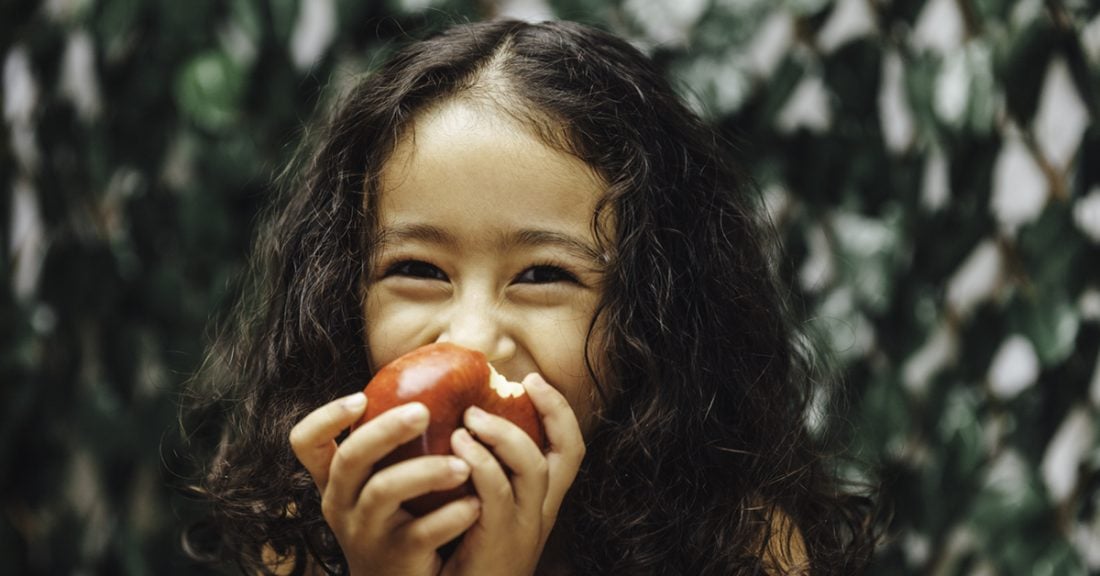 A young girl smiles as she eats a red apple
