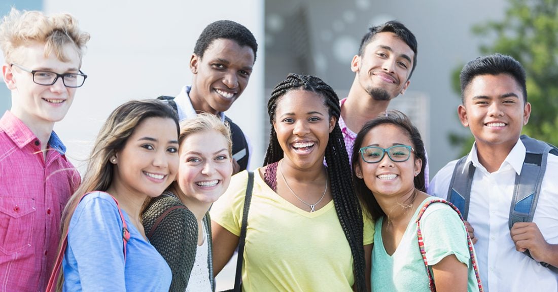 A multicultural group of young people stand smiling at the camera.