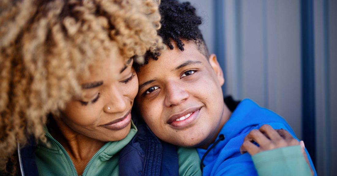 A Black mother and son share a loving embrace. Both smile contentedly.