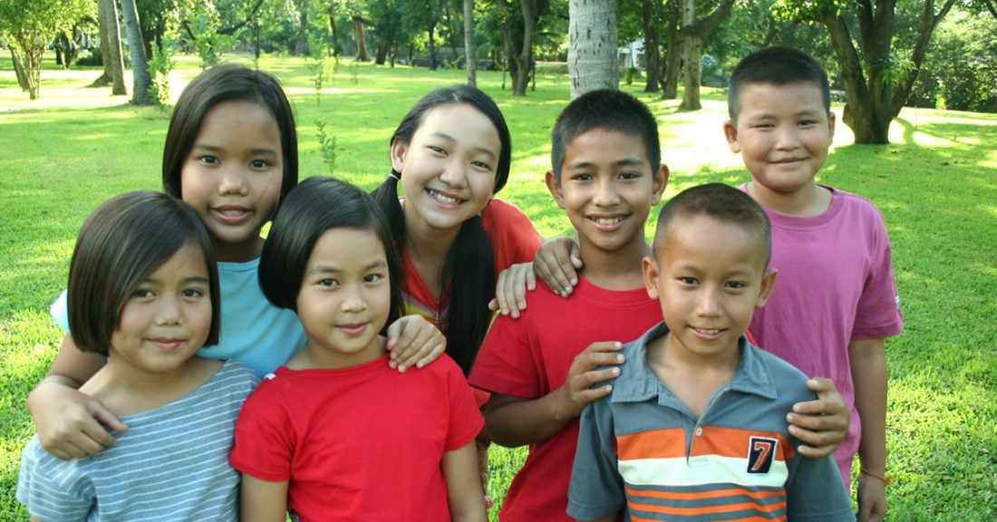 Seven Asian kids take a break from playing in the park to smile for the camera.