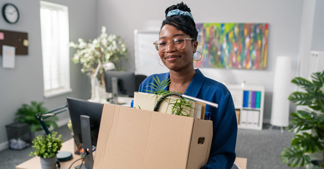 Black young woman holds a box of items from an office.