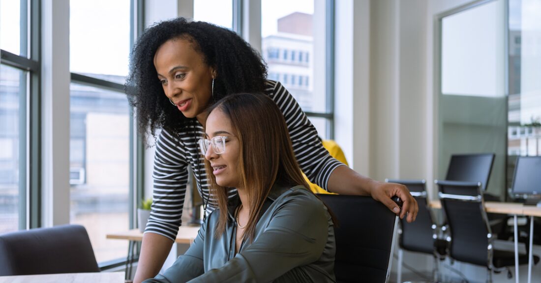 two women look at a computer screen in an office workspace