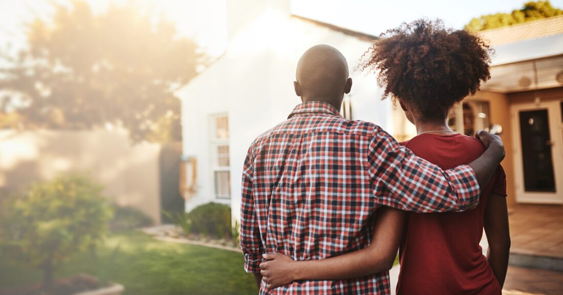 A couple stand outside, looking at a house.