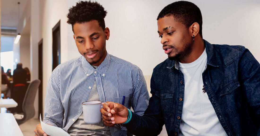 Two young black men review paperwork in an office setting.