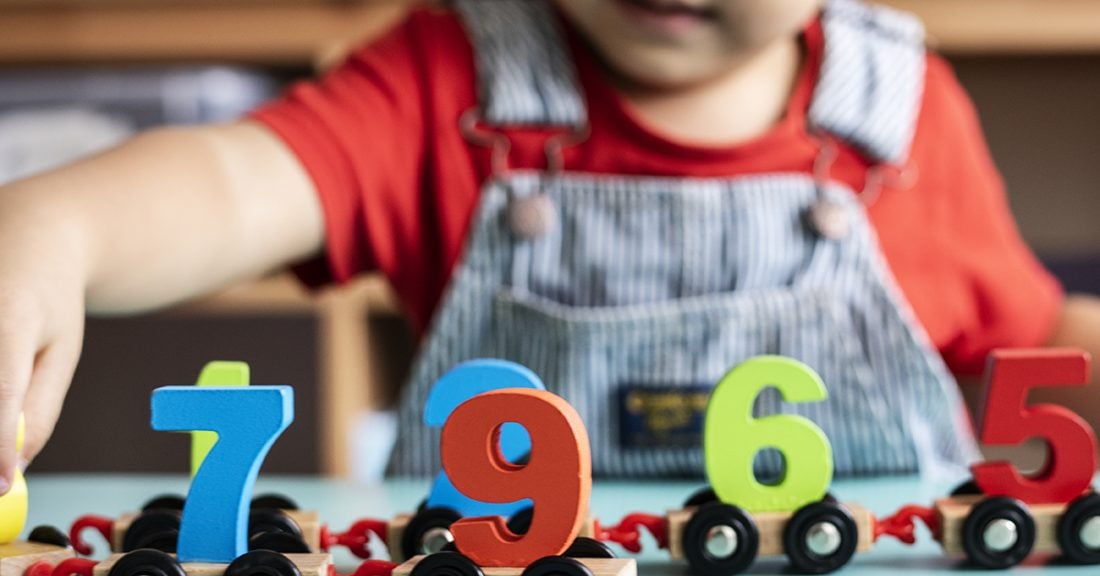 A younng child plays at a table with a train of magnetic wooden numbers