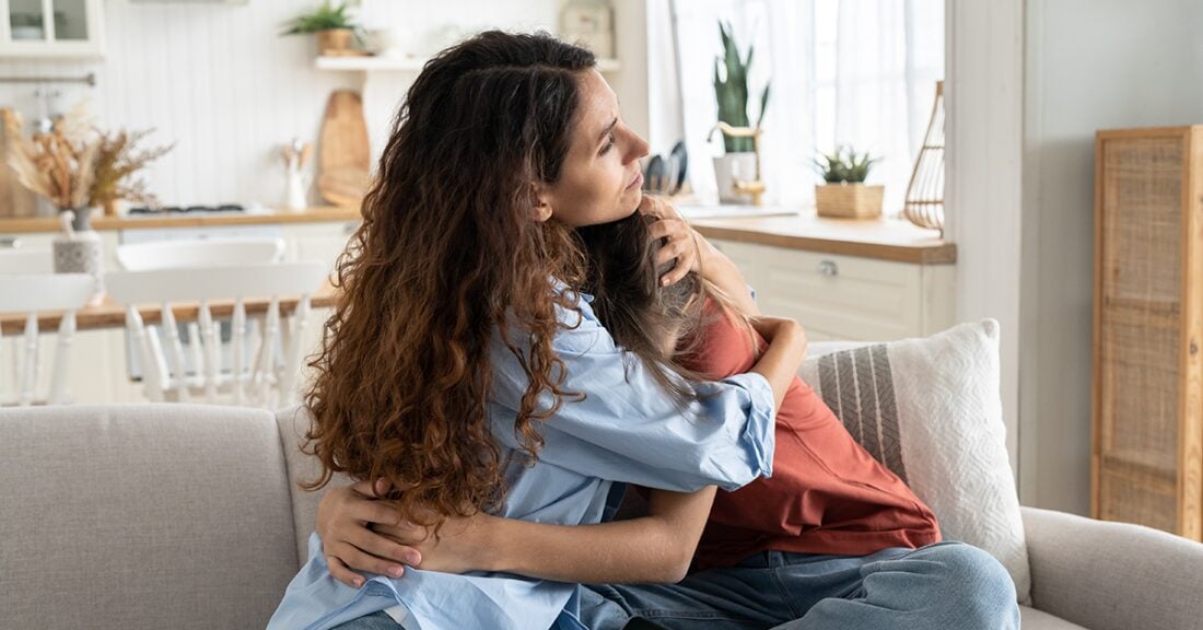 A woman hugs and comforts a young girl on a couch.