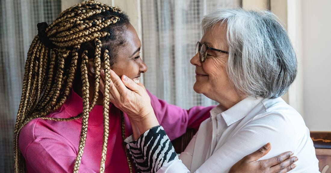 A young Black woman and an older white woman embrace lovingly.