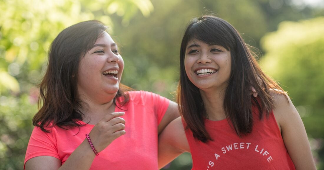 Two young women are outside, laughing as they walk with arms around one another