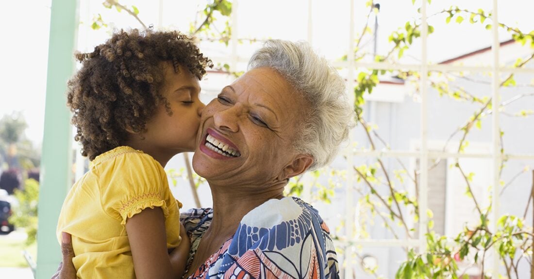 A young black childre kisses her older black gradmother on the cheek; the grandmother is smiling broadly.