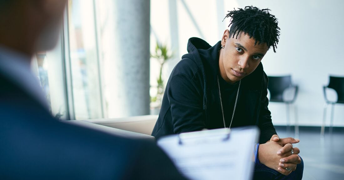 A Black teenage boy speaks with a just-out-of-frame mental health professional during a psychotherapy session.