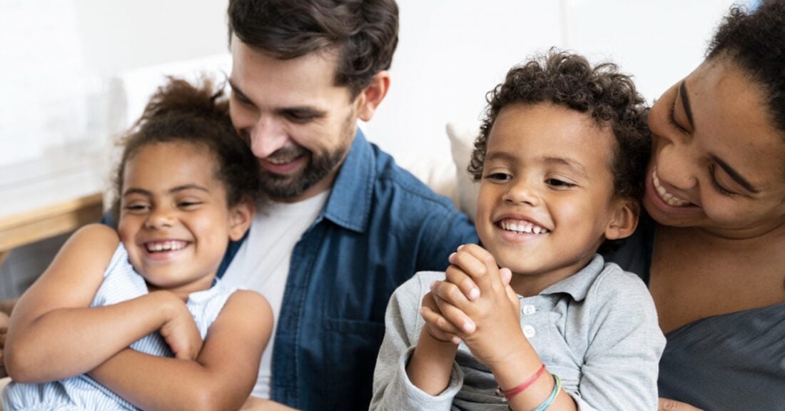 A multiracial family — a father, mother, a son and daughter — share an embrace.