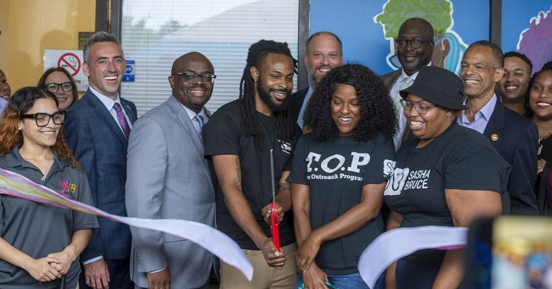 Several members of Baltimore City Youth Action Board participate in a ribbon-cutting ceremony. It's a celebratory mood, those pictured laugh and smile as the ribbon falls.