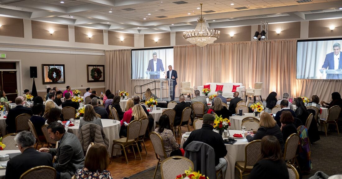 A wide shot of attendees at the Maryland Business Summit. Guests sit at ballroom tables and listen to a speaker who is at the podium in the background.