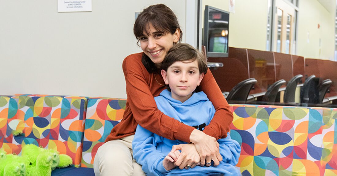 A smiling mom wraps her arms around her son while sitting together on a colorful couch.