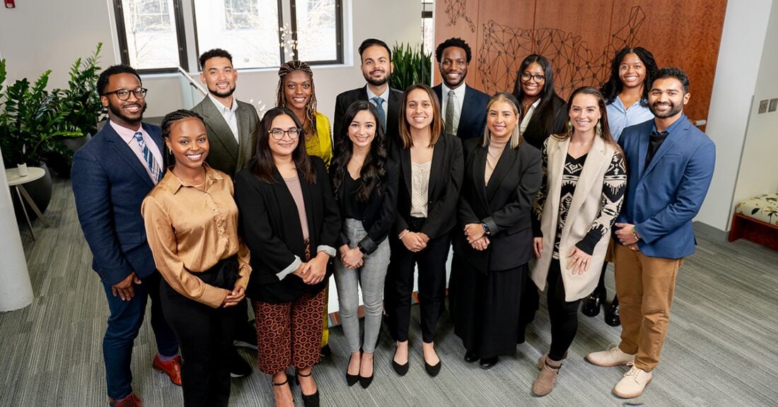 Group photo of 15 diverse professionals standing together in a modern office. They are smiling and dressed in business attire.