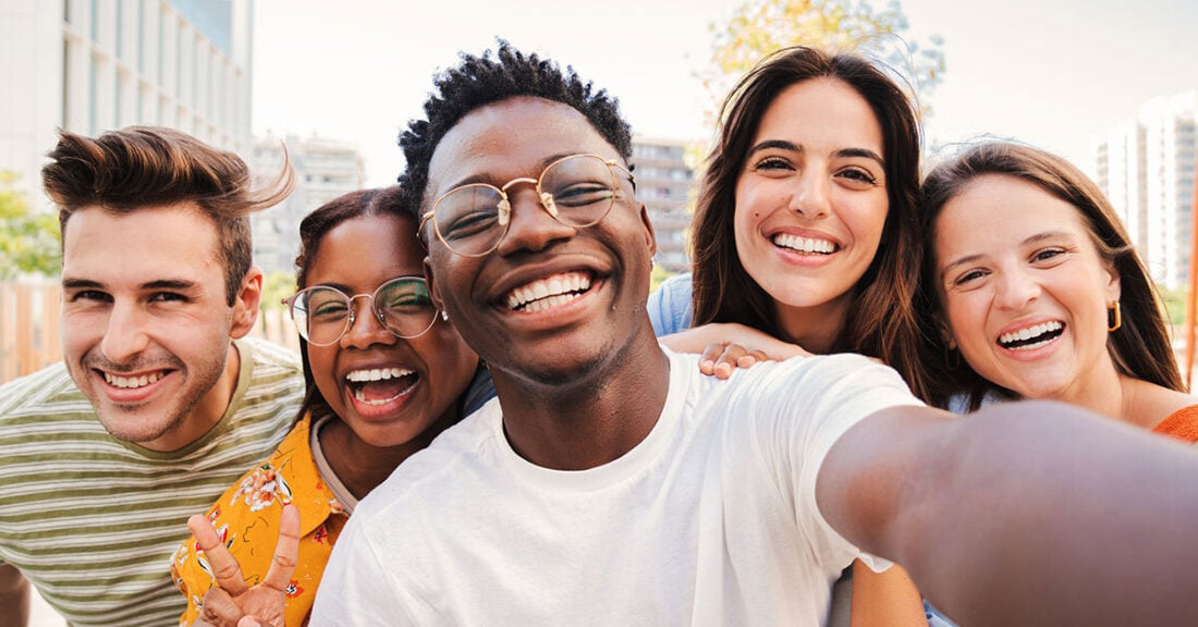 A group of five young adults smiling outdoors, posing closely together for a selfie.