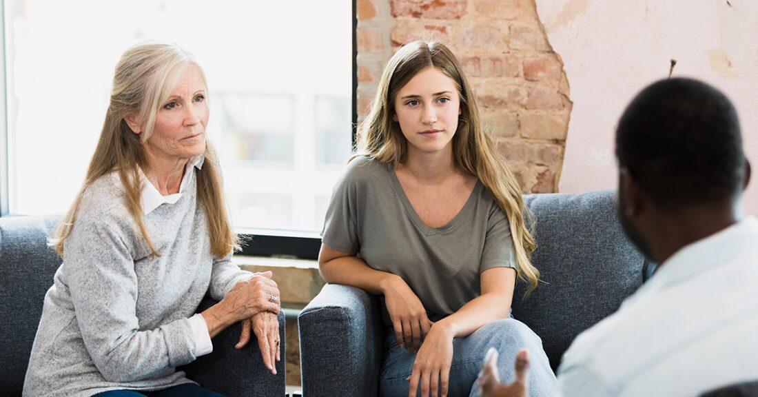 A mom and daughter are seated next to each other, engaged in a conversation with a man who is sitting with his back to the camera.