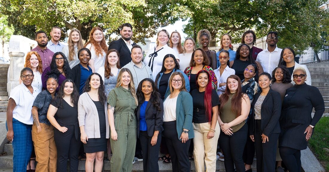 A large group of people, individuals from all backgrounds, stand on steps outdoors, smiling at the camera.