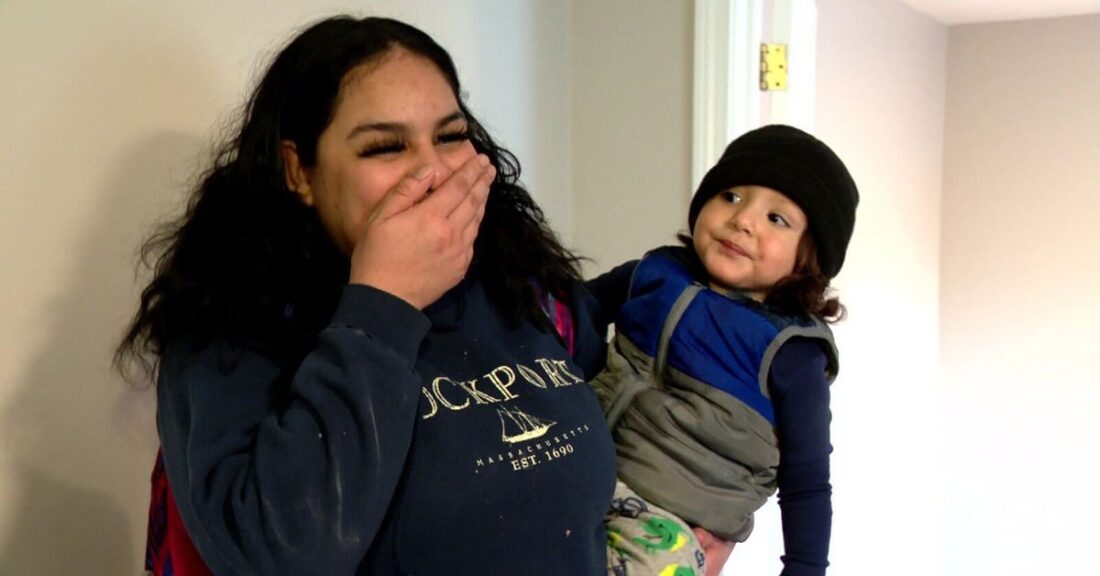 Woman holding a young toddler on her hip, and she's smiling and covering her mouth with her hand, as if in excited shock.