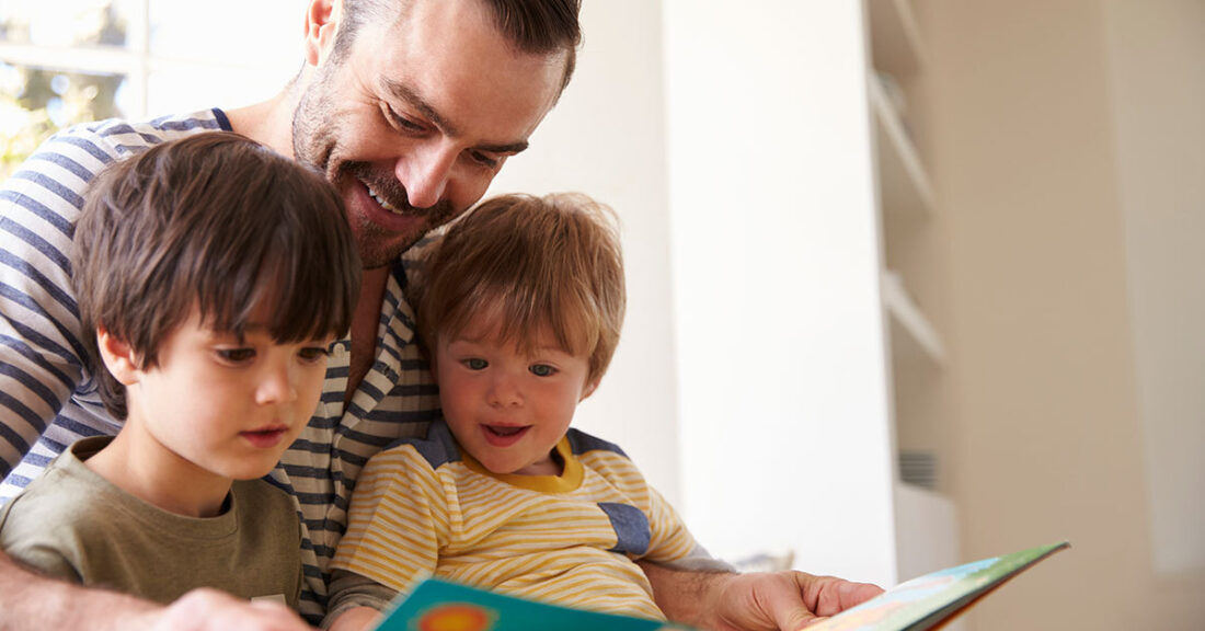 Adult reading a book with two young children.