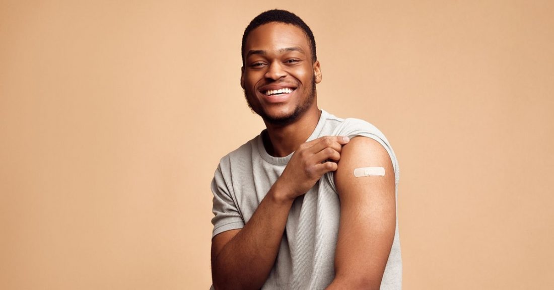 Black male, smiling, with his shirt sleeve up about his shoulder, showing off a bandage on his arm.