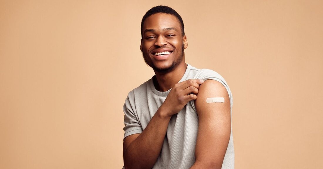 Black male, smiling, with his shirt sleeve up about his shoulder, showing off a bandage on his arm.