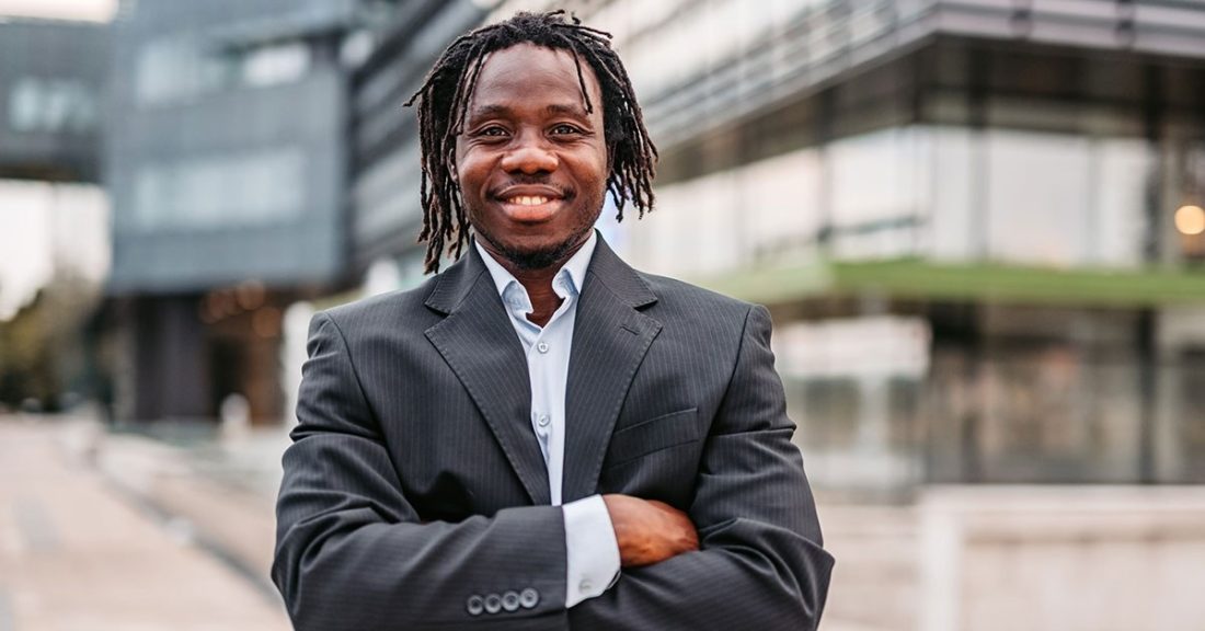 Portrait of young Black businessman with crossed arms outdoors.