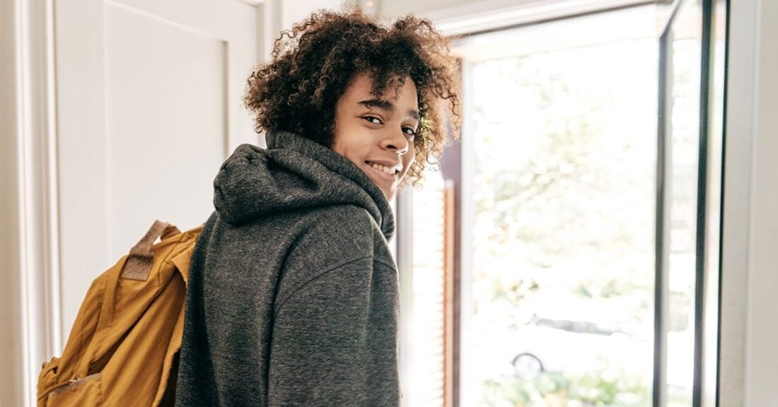 Young man with hoodie and backpack walk out door