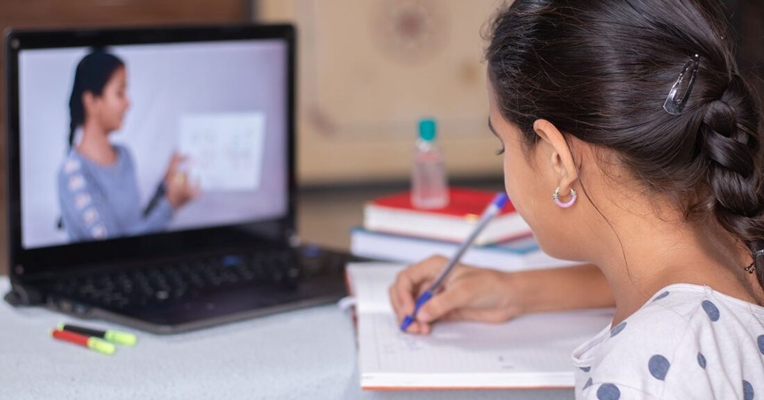 Girl watches lesson on laptop while doing homework