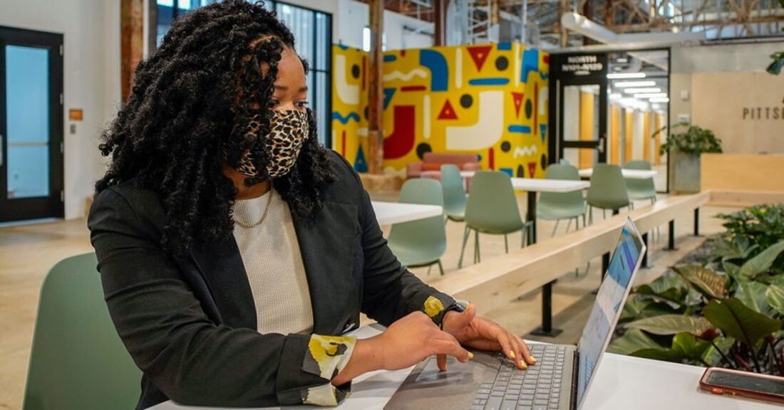 A Black woman sits at a desk and types on a laptop.