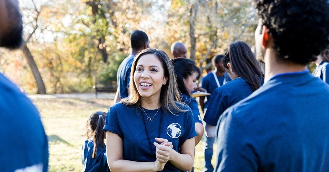 Woman standing outside, smiling, and talking to a group of individuals in matching navy T-shirts.