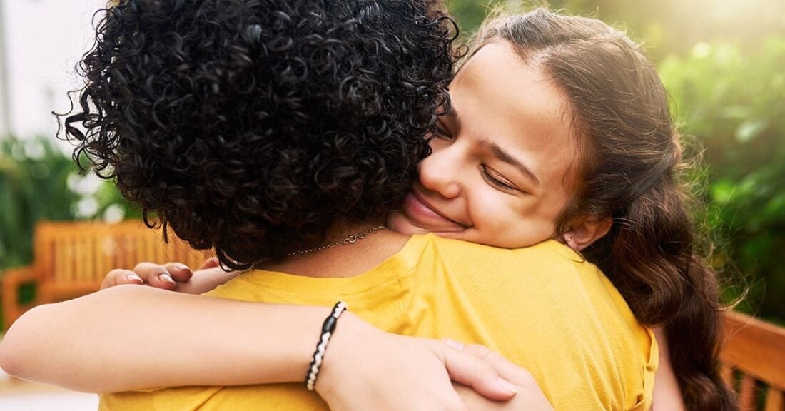 A woman hugs another person, whose back is turned to the camera. The woman is smiling and happy. h