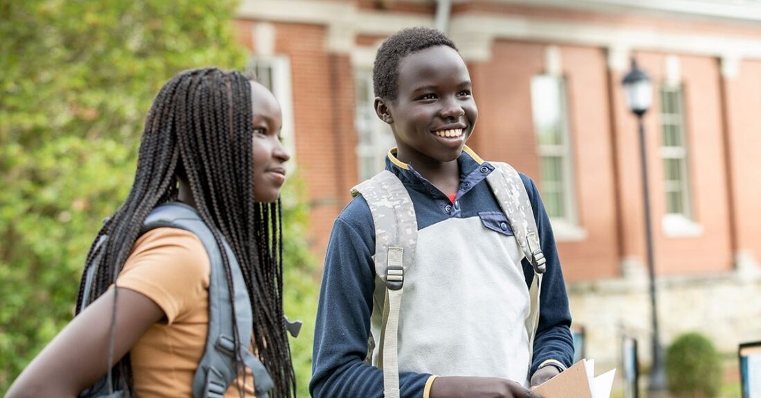 Two Black students are standing outside, wearing bookbags.