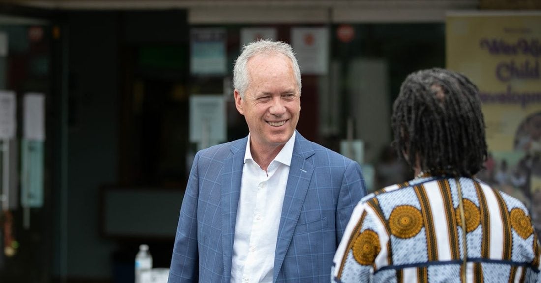 Mayor Greg Fischer smiles while talking to another person whose back is turned to the camera.