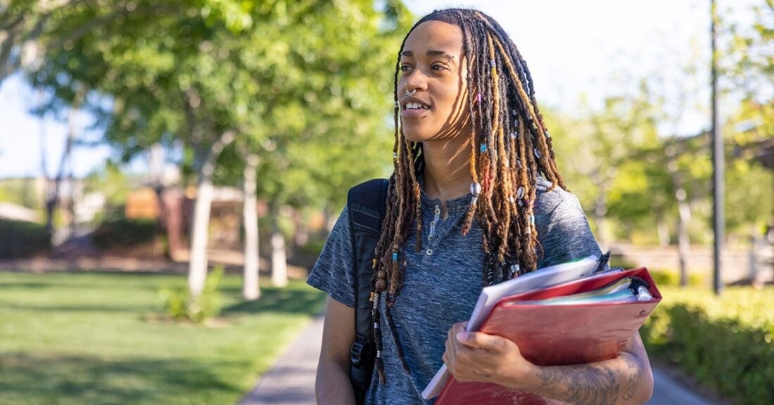 Young person standing outside with a red binder in one hand