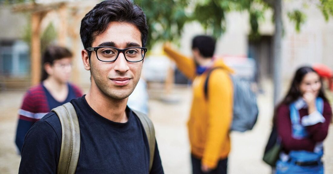 Young person with glasses stands in front of other young people