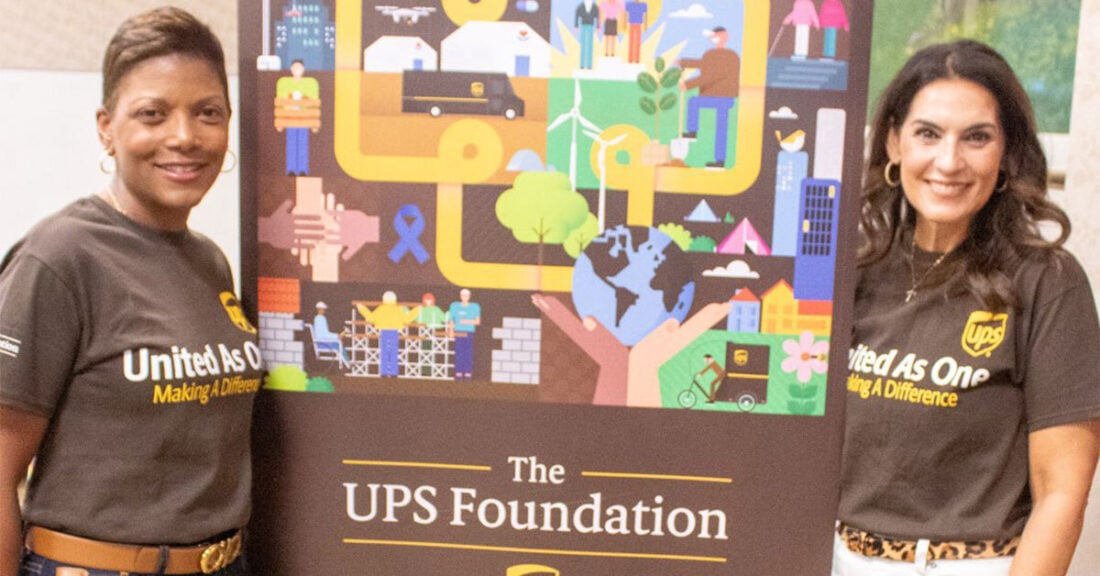 Nicole Clifton stands near UPS Foundation poster with colleague