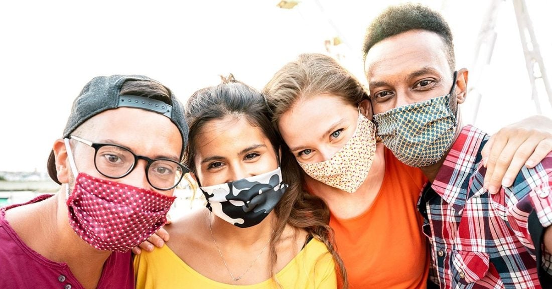 Four young people of different races smile at the camera while wearing masks.