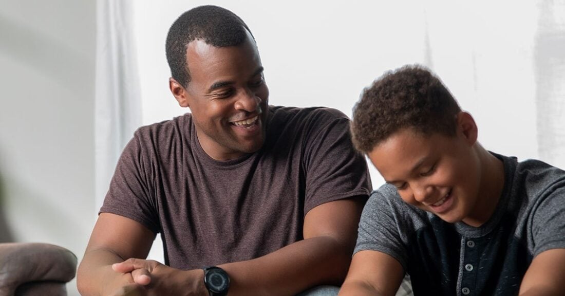 A black man and a black boy are seated next to each other. both are looking down, but smiling.