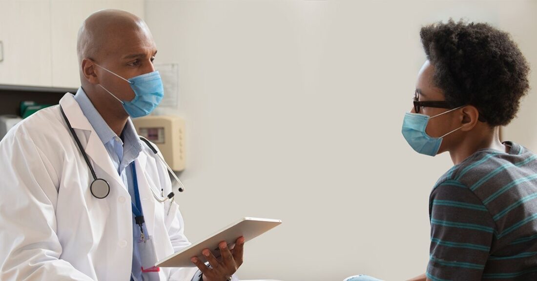 Black doctor with tablet talks with young teen.