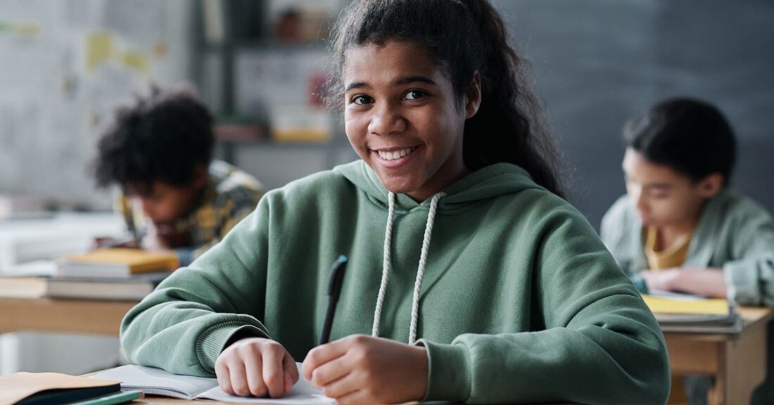 Portrait of African American schoolgirl smiling at camera sitting at her desk with books during a lesson