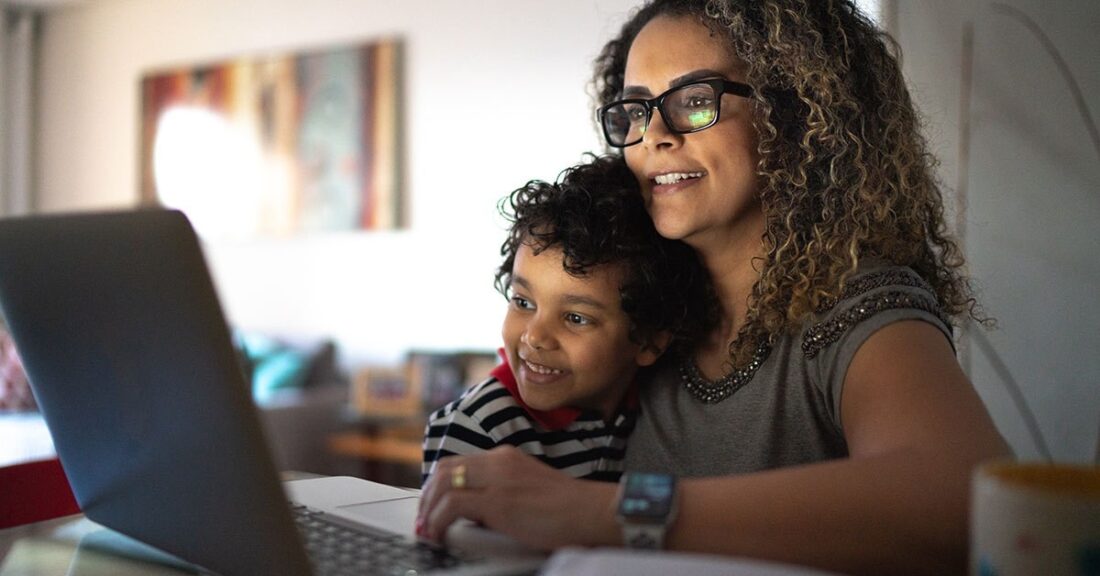 Woman holds her son close on her lap as they both look at something on a laptop screen.